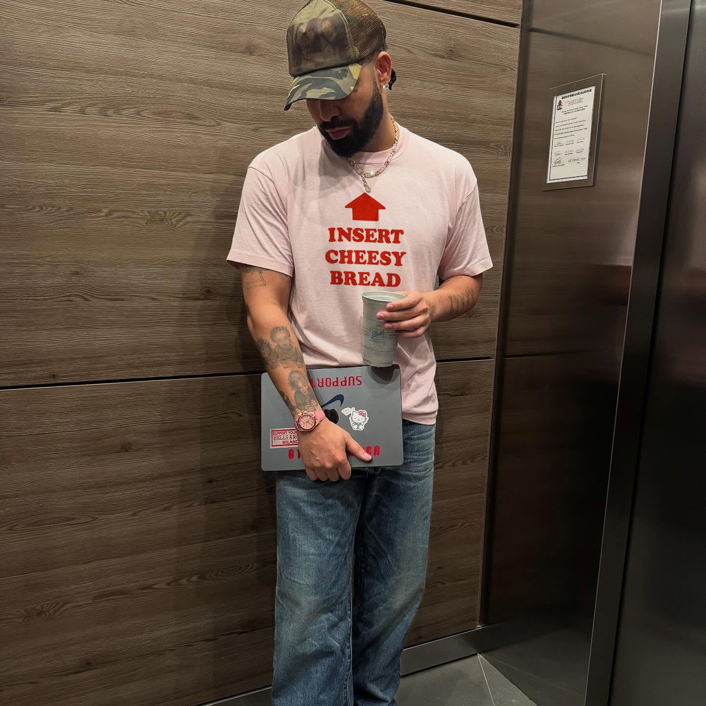 Person wearing a t-shirt with text "Insert Cheesy Bread" standing next to a refrigerator.