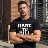 Man wearing a black t-shirt with 'HARD TO KILL' text, standing against a brick wall.