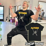 Person wearing a black t-shirt with 'AUTISM' and a skeleton design, standing in a room with chairs and a counter.